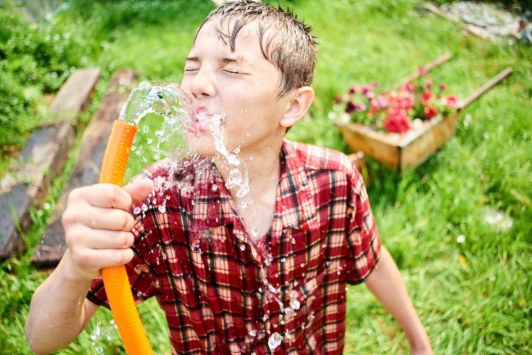 The guy in the wet clothes drinking water from a hose on the farm
